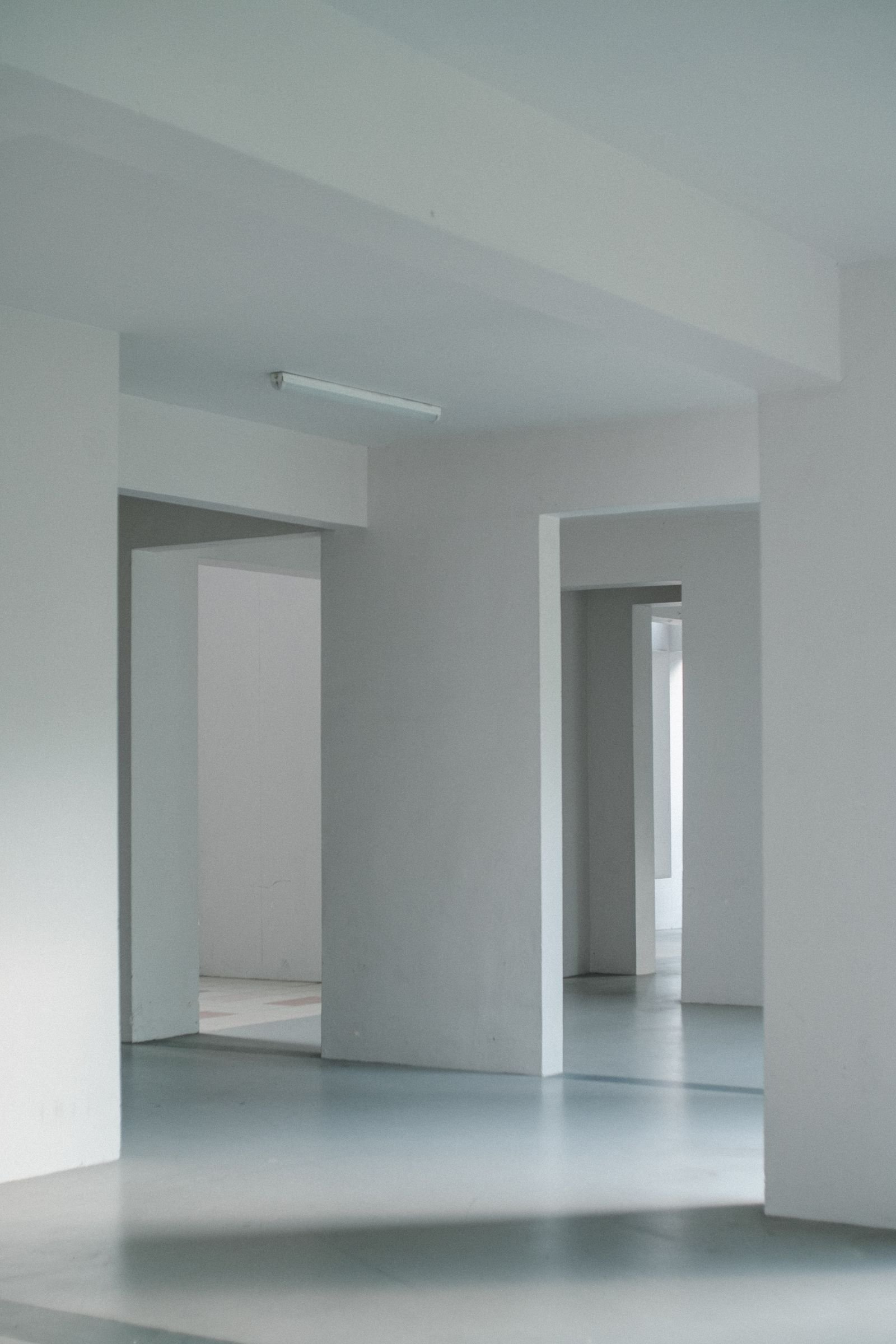 Intérieur entièrement vide aux murs et plafonds blancs, sol clair, enfilade de deux ouvertures sans porte, sans aucun mobilier.