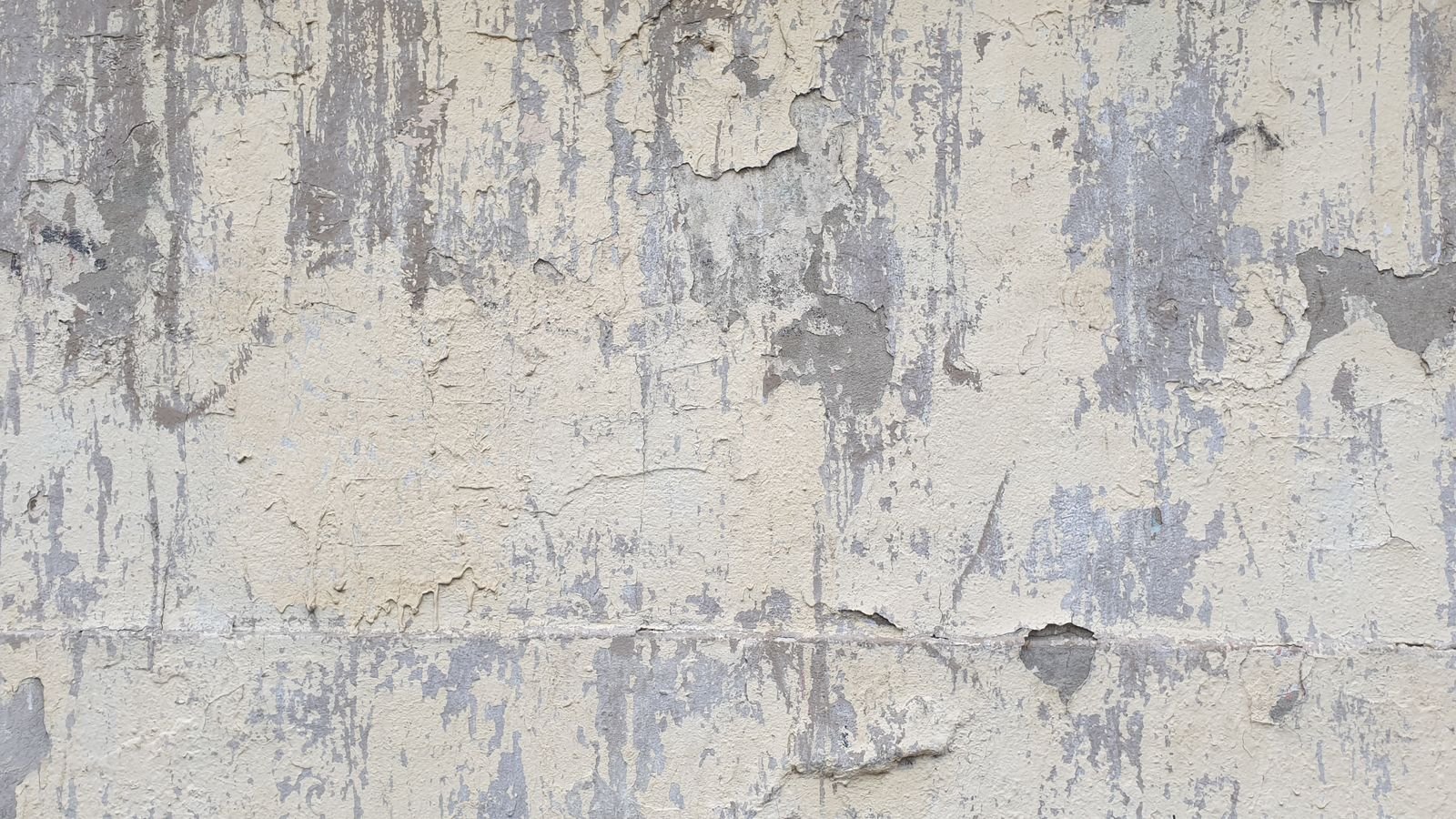 Détail d'un mur de béton clair marqué de coulures et de zones plus sombres, enduit partiellement disparu.