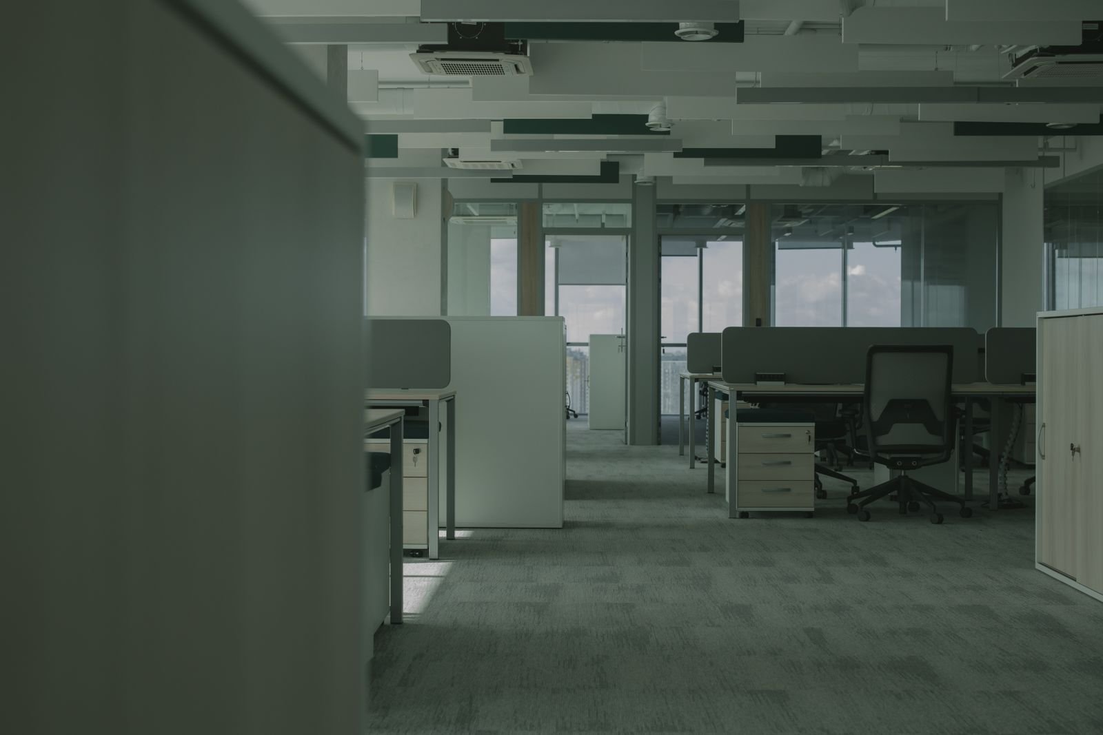 Plateau de bureaux vide vu depuis un couloir, postes de travail séparés par des cloisons basses, moquette et faux plafond technique.